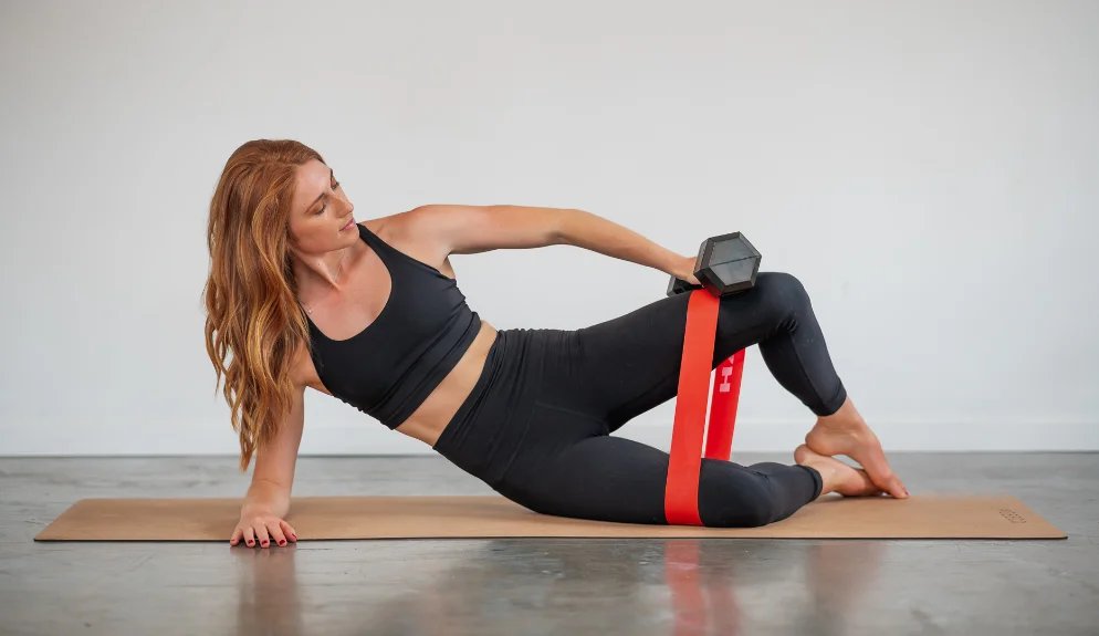 Bridget doing a side-lying Pilates exercise with a resistance band and dumbbell